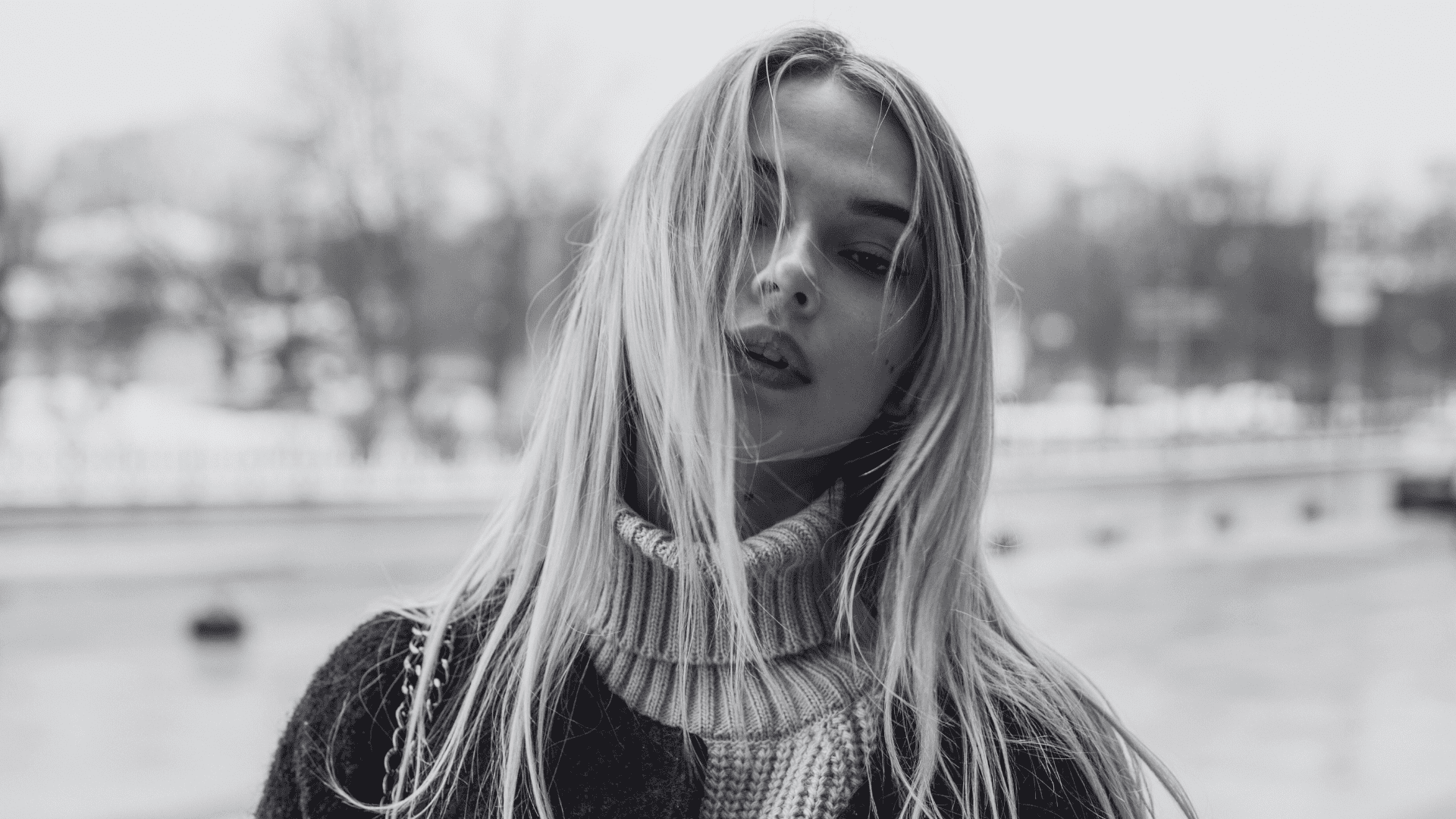 Young woman with long hair in urban winter setting, wearing a turtleneck and coat.